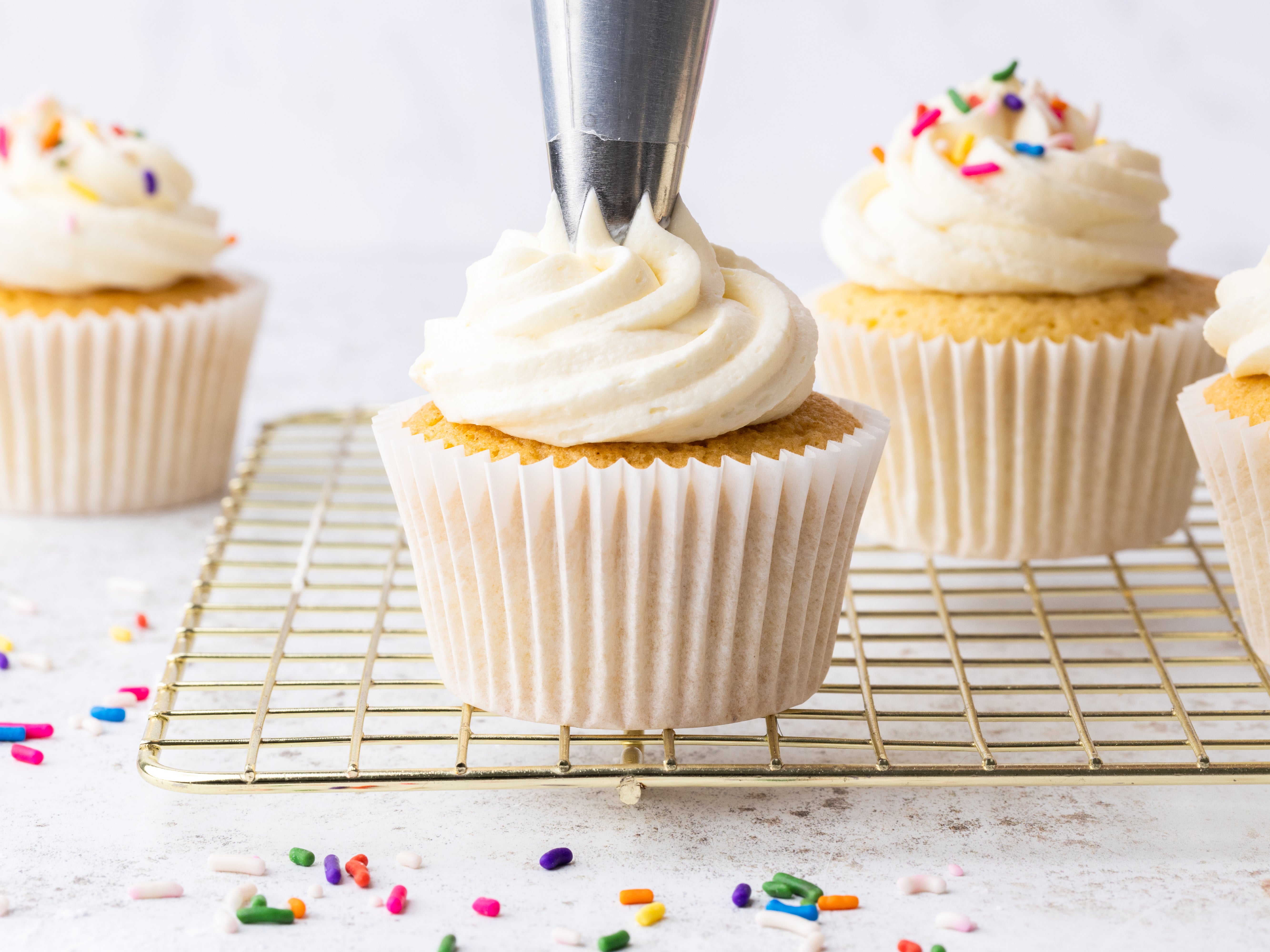 Close up of vanilla being piped on top of a cupcake