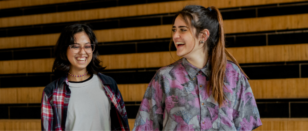 Twee studentes lopen lachend door de gang.