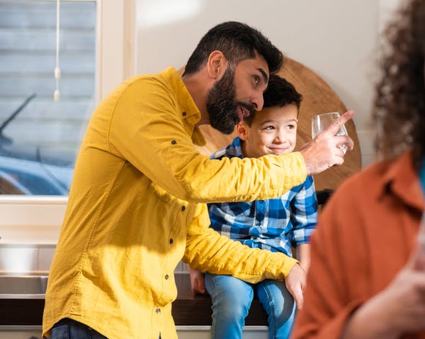 Man in geel hemd met glas en jongen op aanrecht