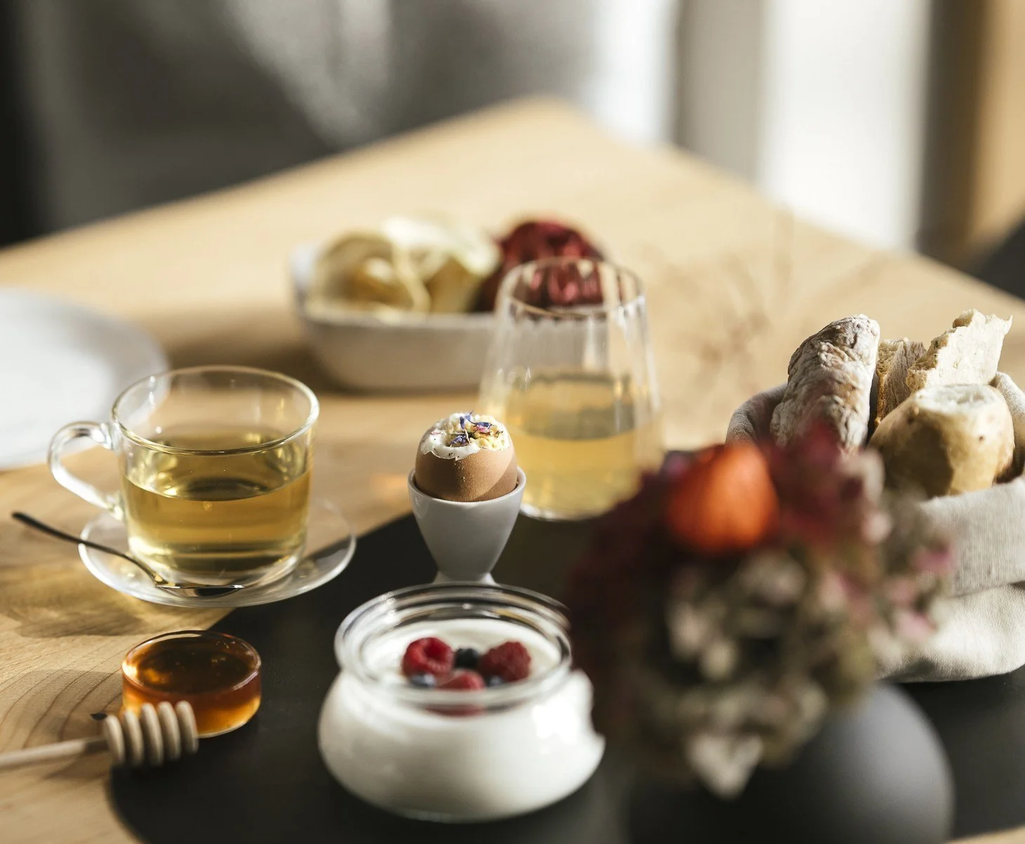 Der Tisch ist mit einem Frühstück aus Tee, Joghurt mit Beeren, Honig, Brot und einem gekochten Ei gedeckt.
