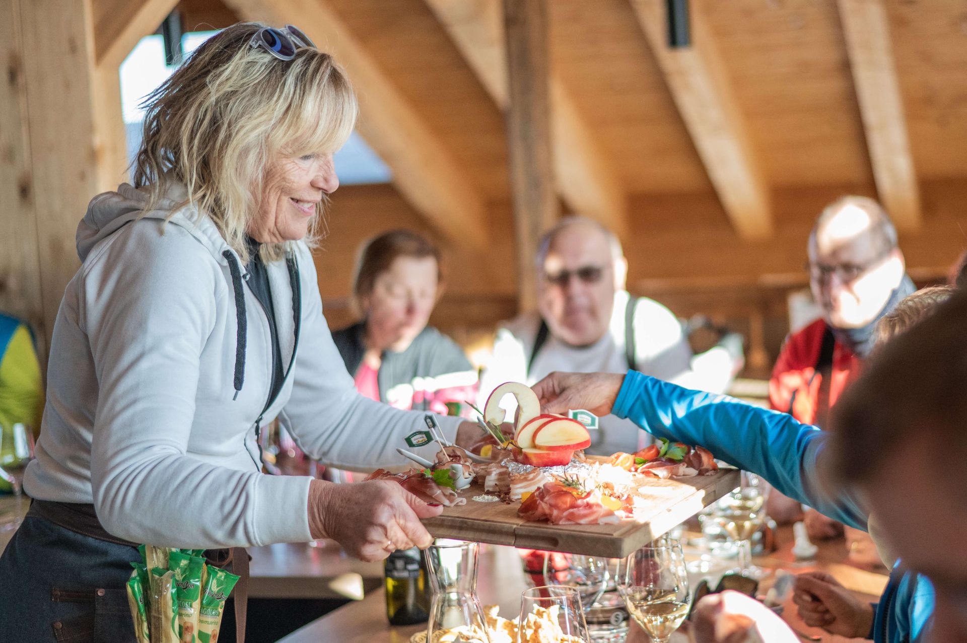 Frau serviert Brett mit Häppchen mit Speck Alto Adige g.g.A. an Tisch mit mehreren Personen
