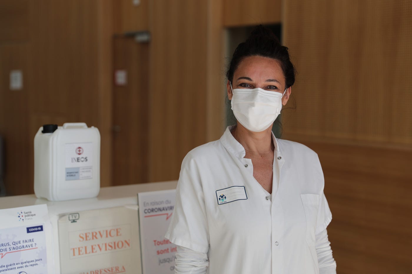 a woman in a white uniform and mask smiling at the camera