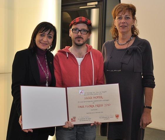 Auf dem Foto von links nach rechts zu sehen: Tirols Kulturlandesrätin Beate Palfrader, Siggi Hofer mit der Preisurkunde und Südtirols Kulturlandesrätin Sabina Kasslatter Mur in der Taxisgalerie in Innsbruck. Foto: Land Tirol.