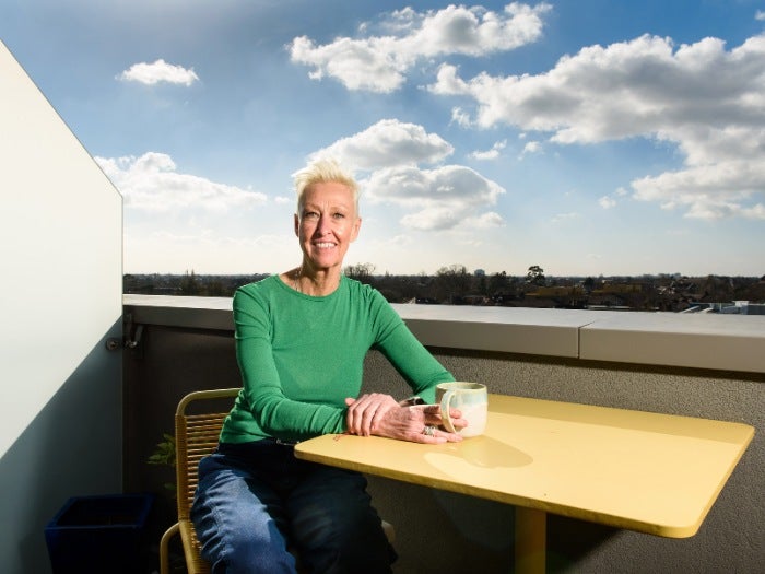 Moira sits with a coffee at her table on her balcony 