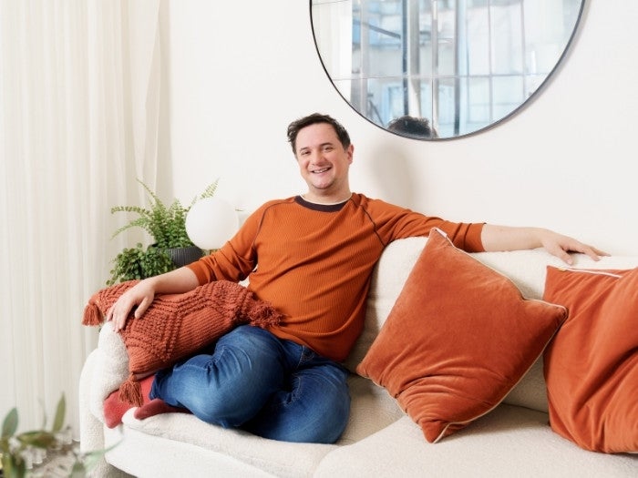 Matthew smiles as he relaxes on his sofa in his living room.