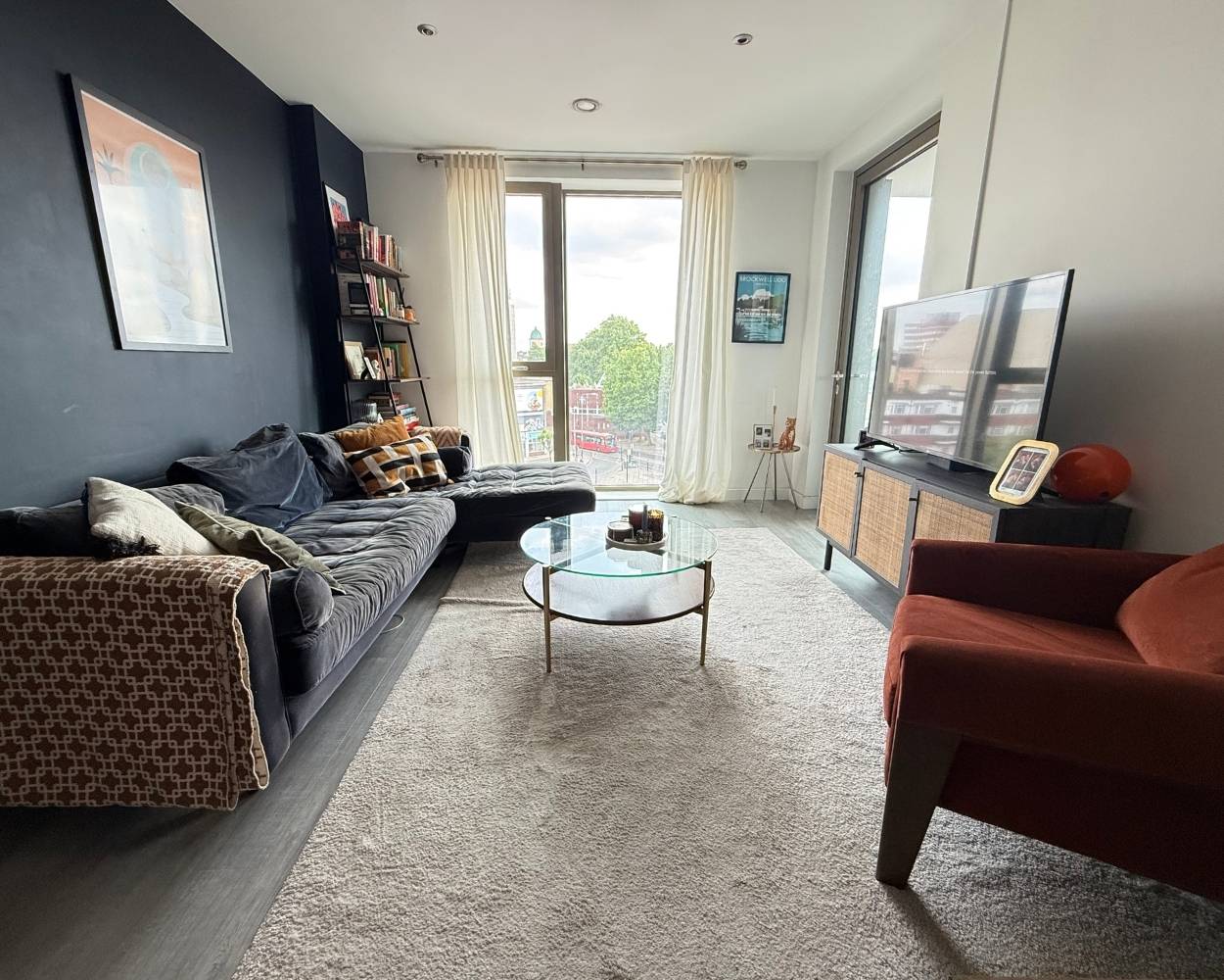 Photo of the living area featuring 3 seater corner sofa, stylish dark orange chair, floor to ceiling windows and door to the balcony space