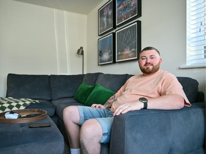 Ethan smiles as he sits for a picture on his dark grey sofa.