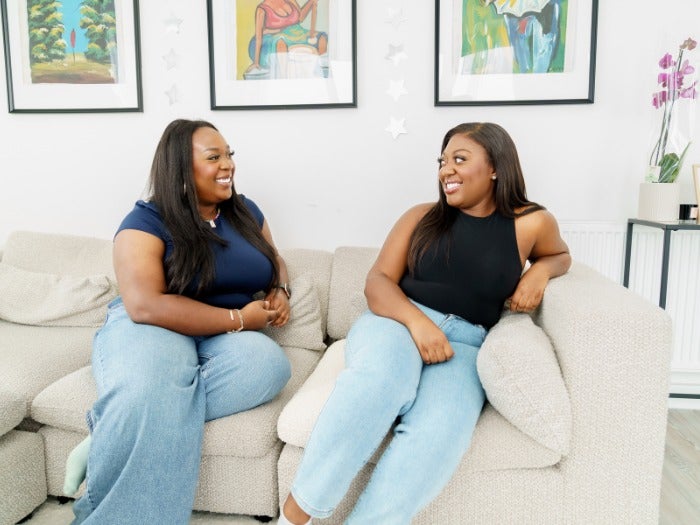 Baaba and Josephine smile at each other as they sit on the sofa together