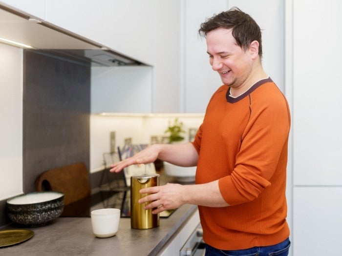 Matthew smiles as he makes a coffee using his gold cafetiere in his kitchen.