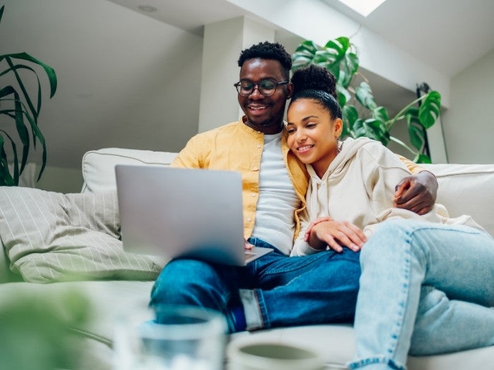 A couple relax on their sofa whilst using a laptop