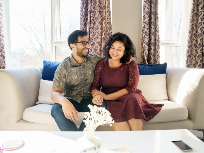 Anindya & Oishani pose for a picture sat on their sofa in their living room.