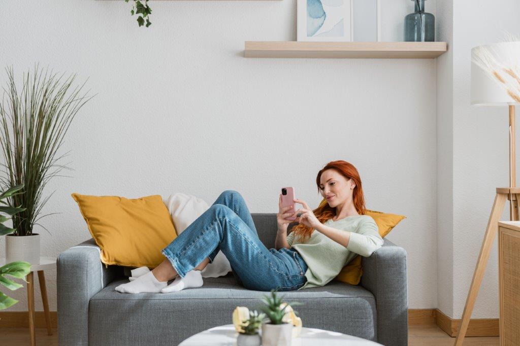 Woman relaxes on the sofa as she scrolls on her smartphone.