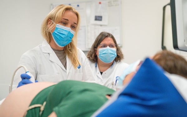 Twee zorgverleners staan naast een patiënt die op bed ligt.