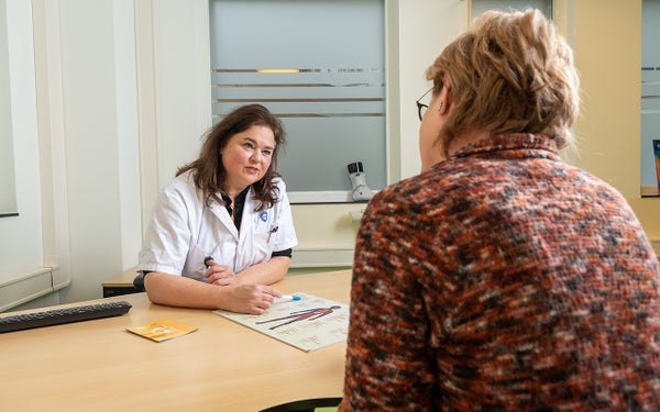 Een zorgverlener praat met een patiënt in een kamer.