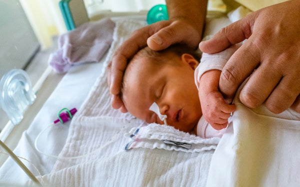 Verzorgende legt handen op een baby in een bedje