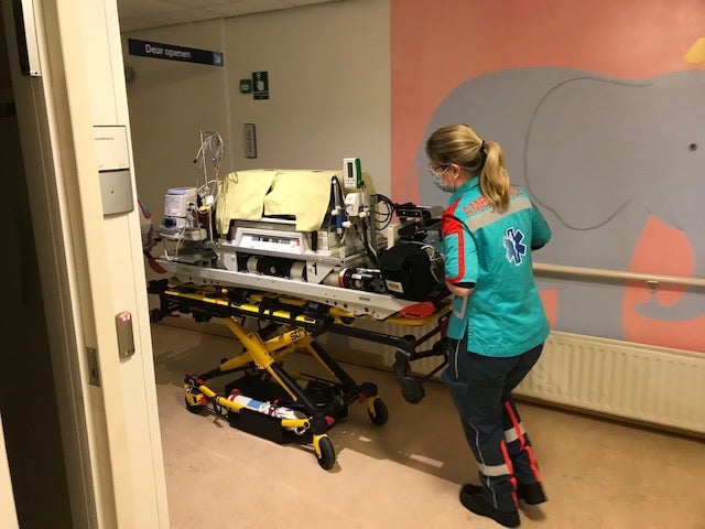 Ambulanceverpleegkundige duwt brancard met couveuse
