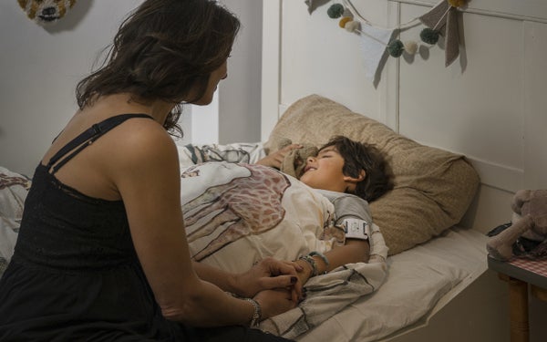 Moeder houdt de hand van kind vast, die in bed ligt.