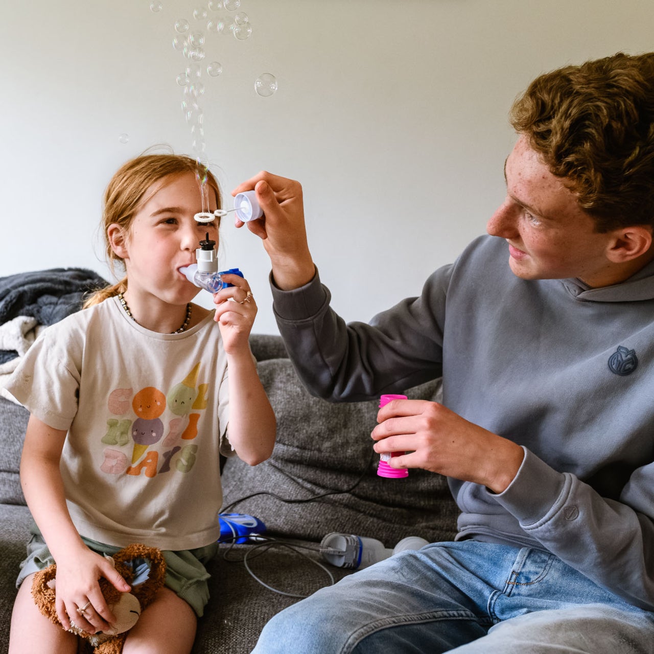 Veerle heeft cystic fibrosis (CF) en neemt medicijnen met een pufje in. Haar broer houdt een bellenblaas boven de uitlaat van het pufje, zodat er bubbels verschijnen.