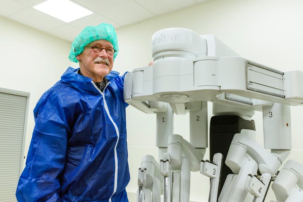 Man in operatiekleding staat vrolijk kijkend naast Da Vinci 5 robot