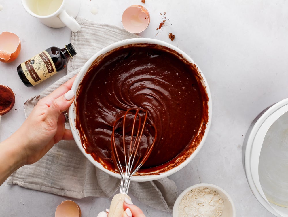 Chocolate cake mix being whisked in a bowl surrounded by baking ingredients