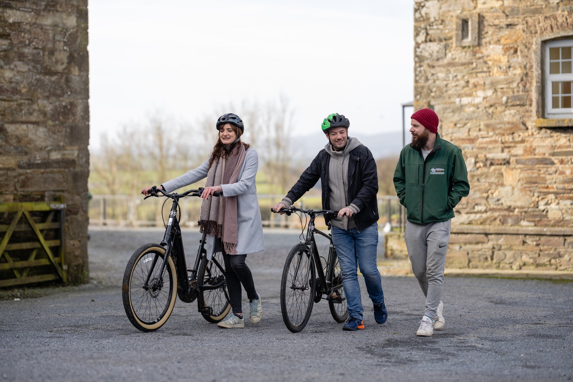 Three people walking with e-bikes outside a traditional stone building in the Irish countryside