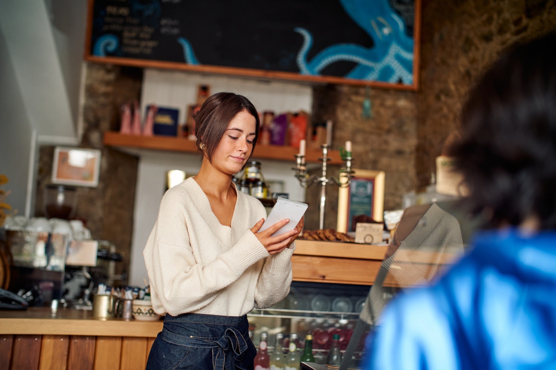 Café staff member writing in a notepad while serving a customer at a counter