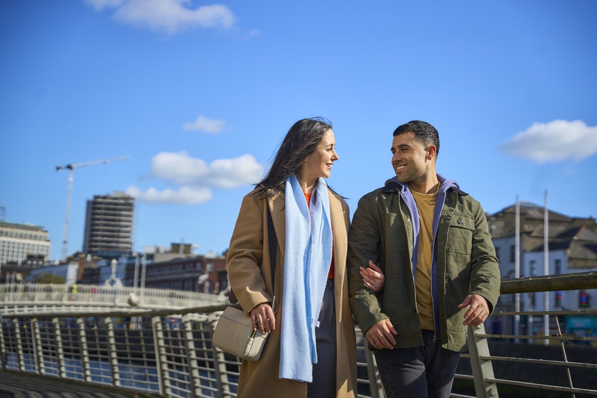 A couple walking arm-in-arm across a bridge in Dublin city centre on a bright sunny day with a blue sky.