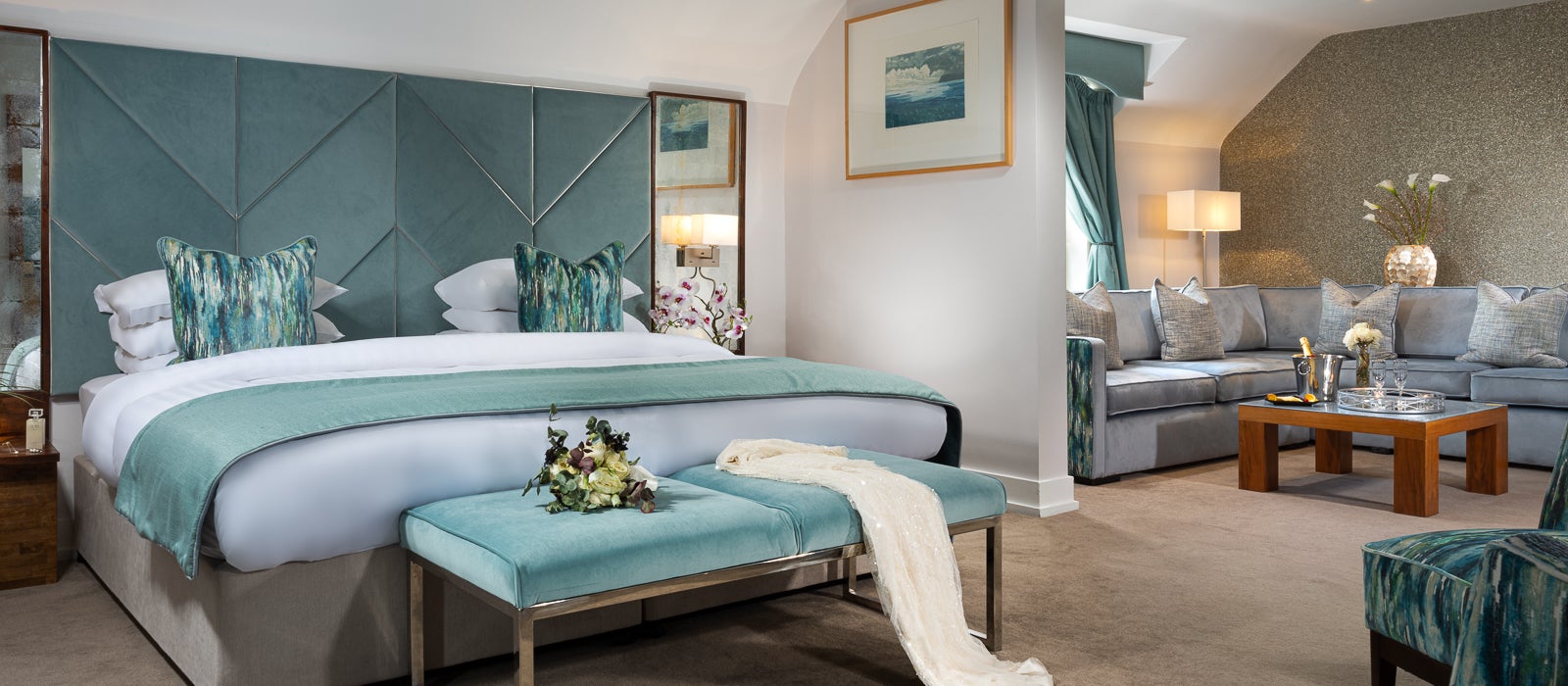 Luxury hotel bedroom with a teal velvet headboard, crisp white linen, and an adjacent seating area