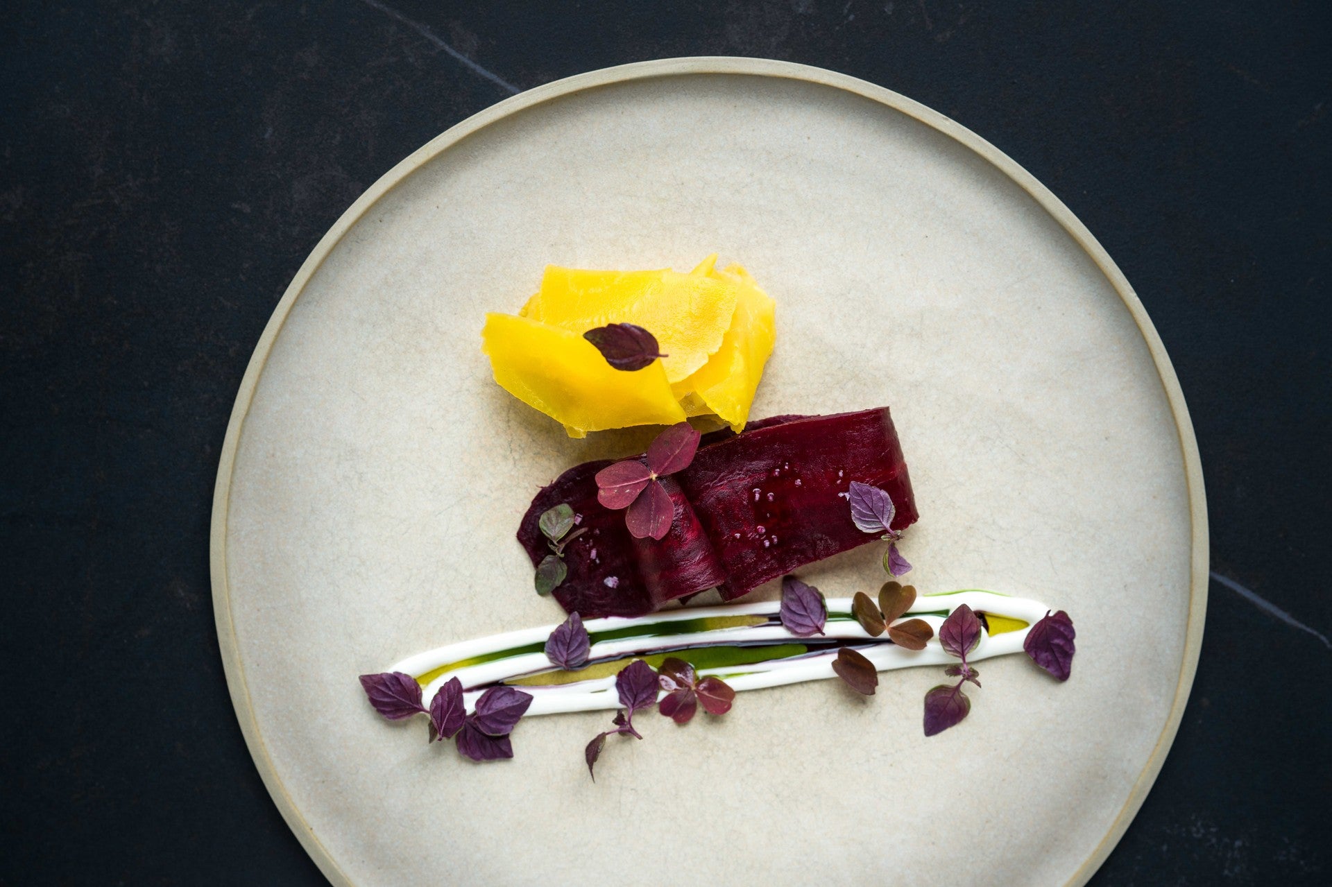 Fine dining plate with roasted beetroot, golden beetroot, and herb and cream garnish on a ceramic dish