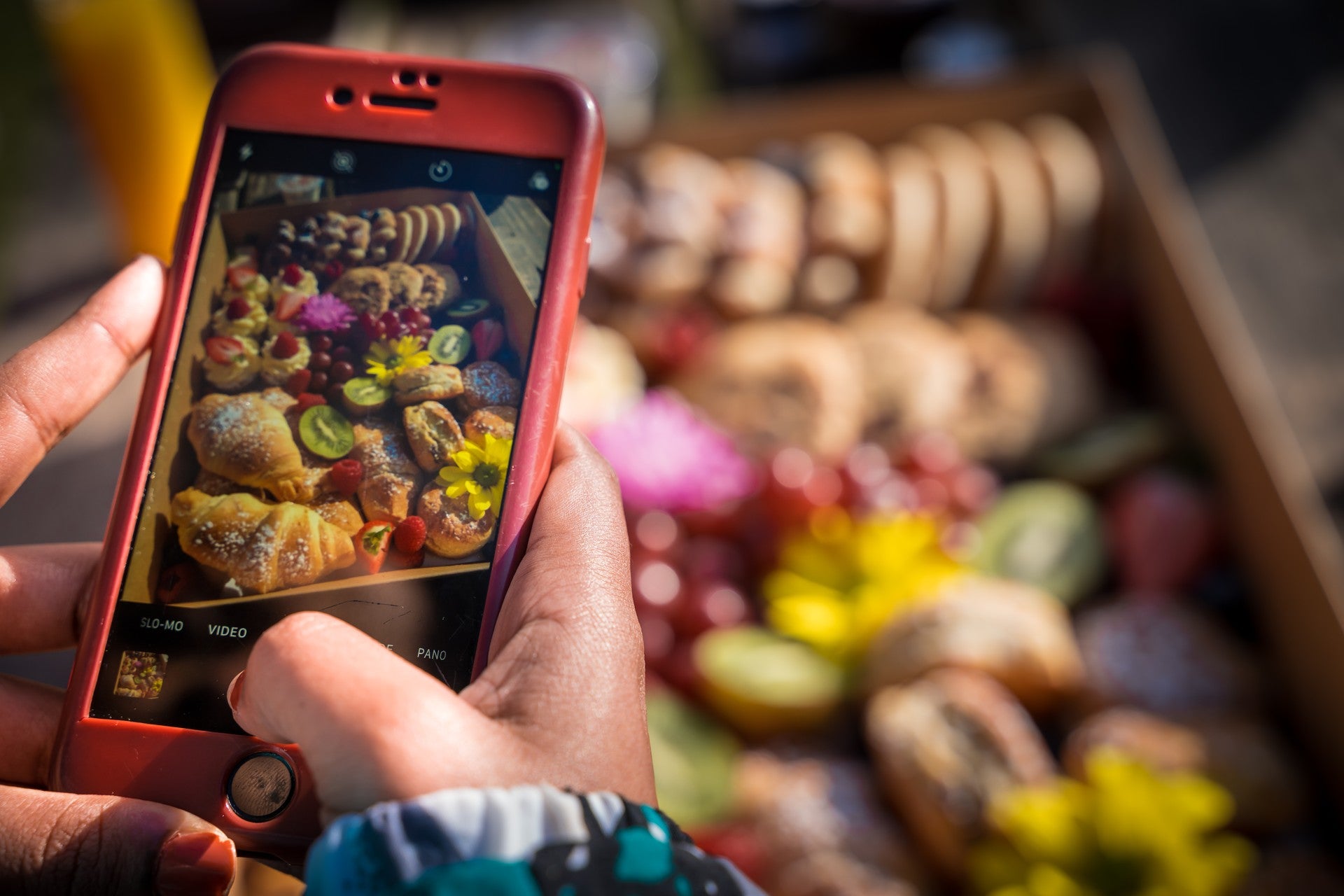 Person photographing a colourful arrangement of pastries and fruit at an outdoor market using a smartphone