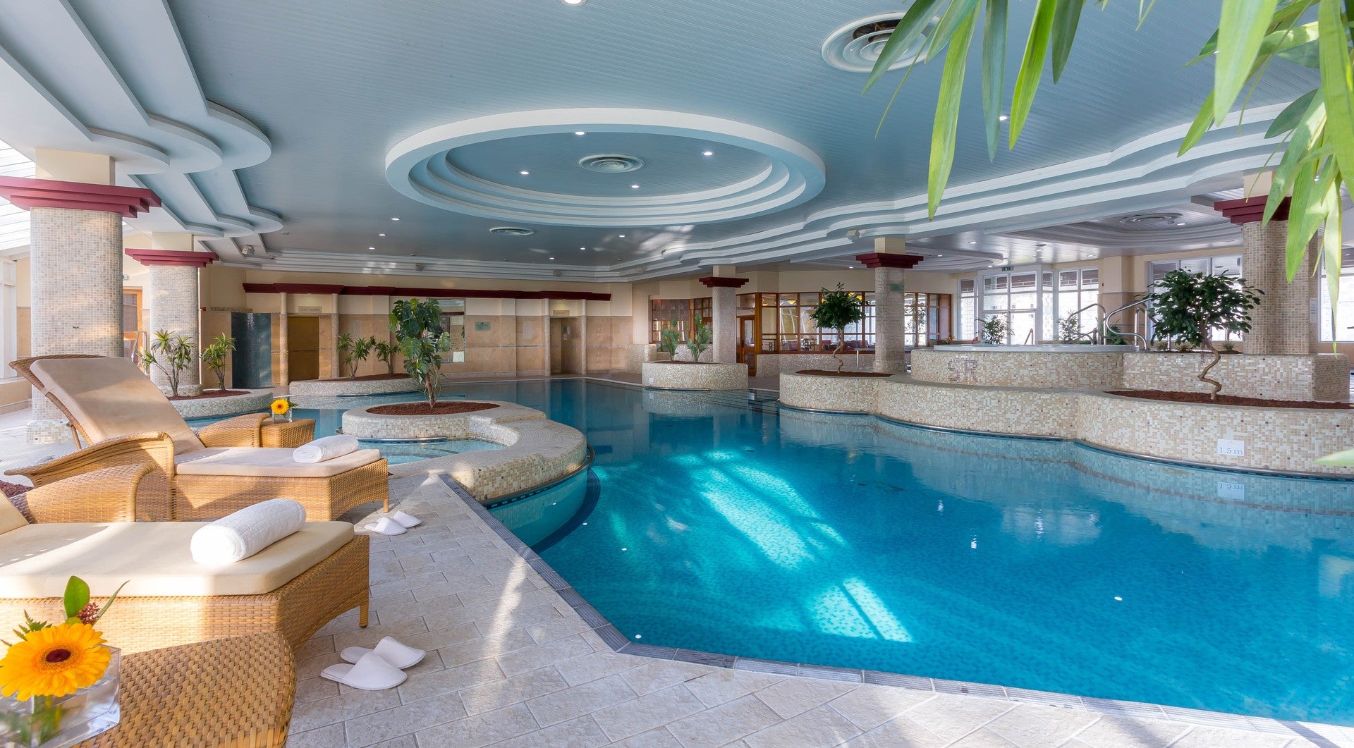 Luxury hotel indoor swimming pool with wicker sun loungers, white towels, and tropical plants