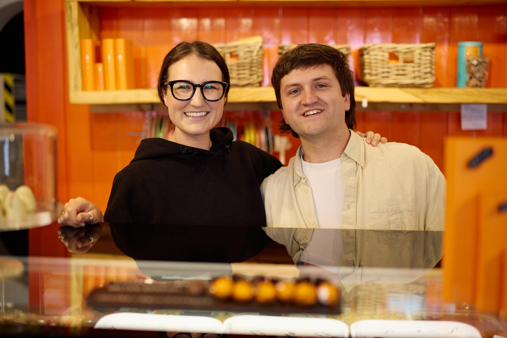 Two young people smiling behind the counter of a colourful confectionery shop