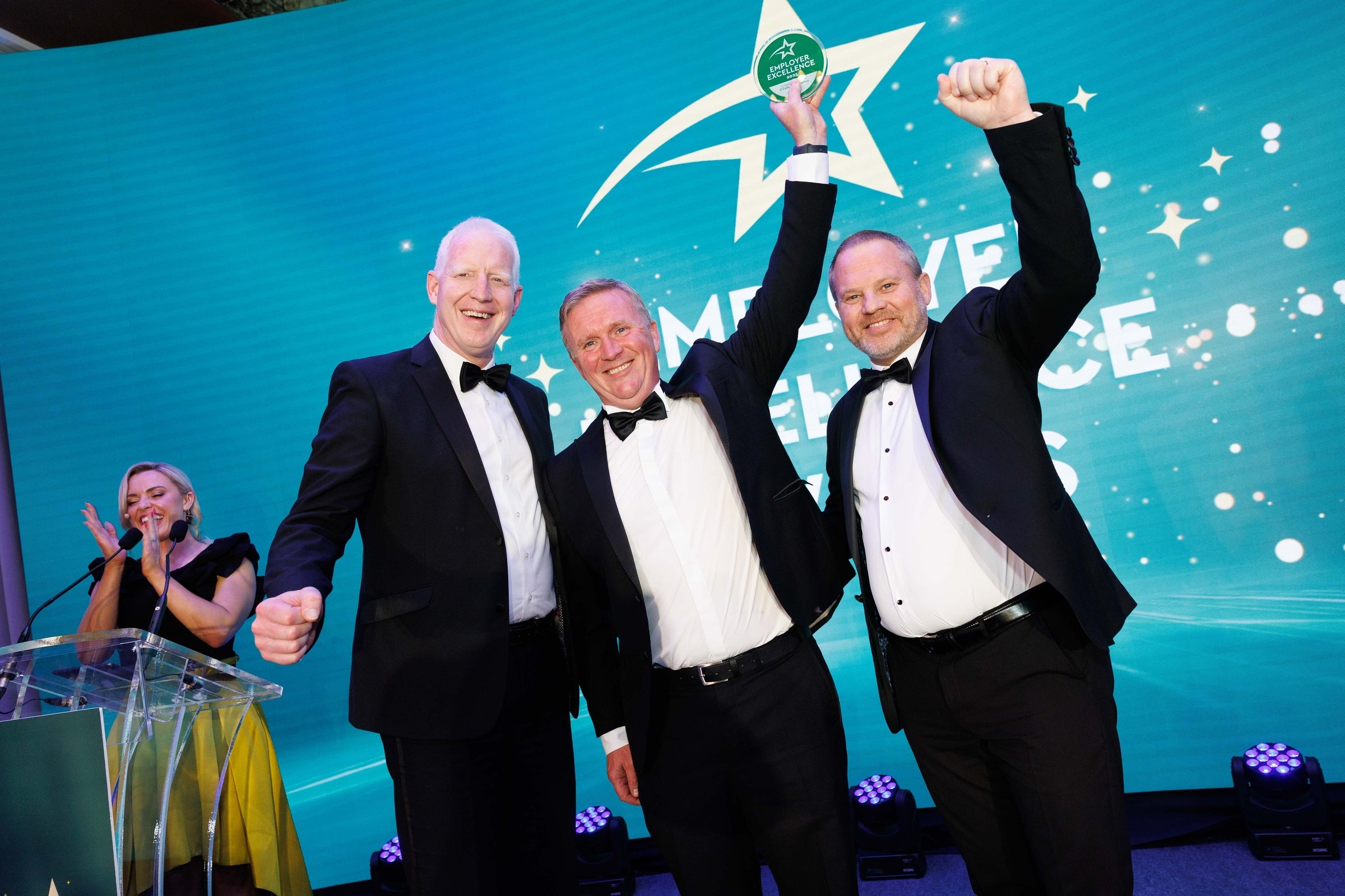 Winners of the employer excellence awards pose for a photo raising fists to the air.
