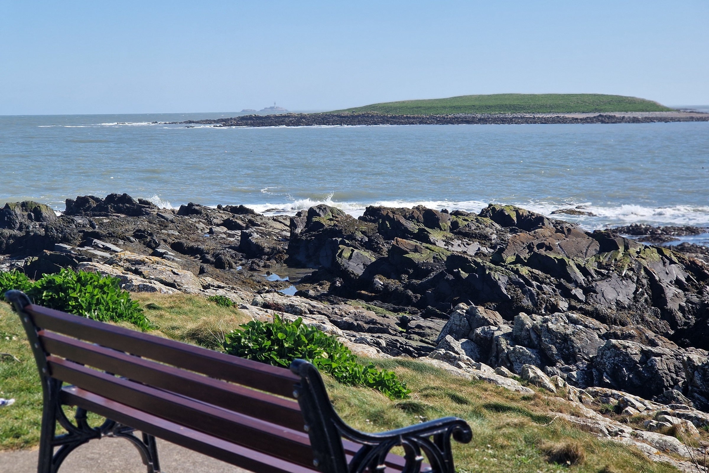 An outdoor bench looking out on Dublin's rocky shoreline and an island in the distance.