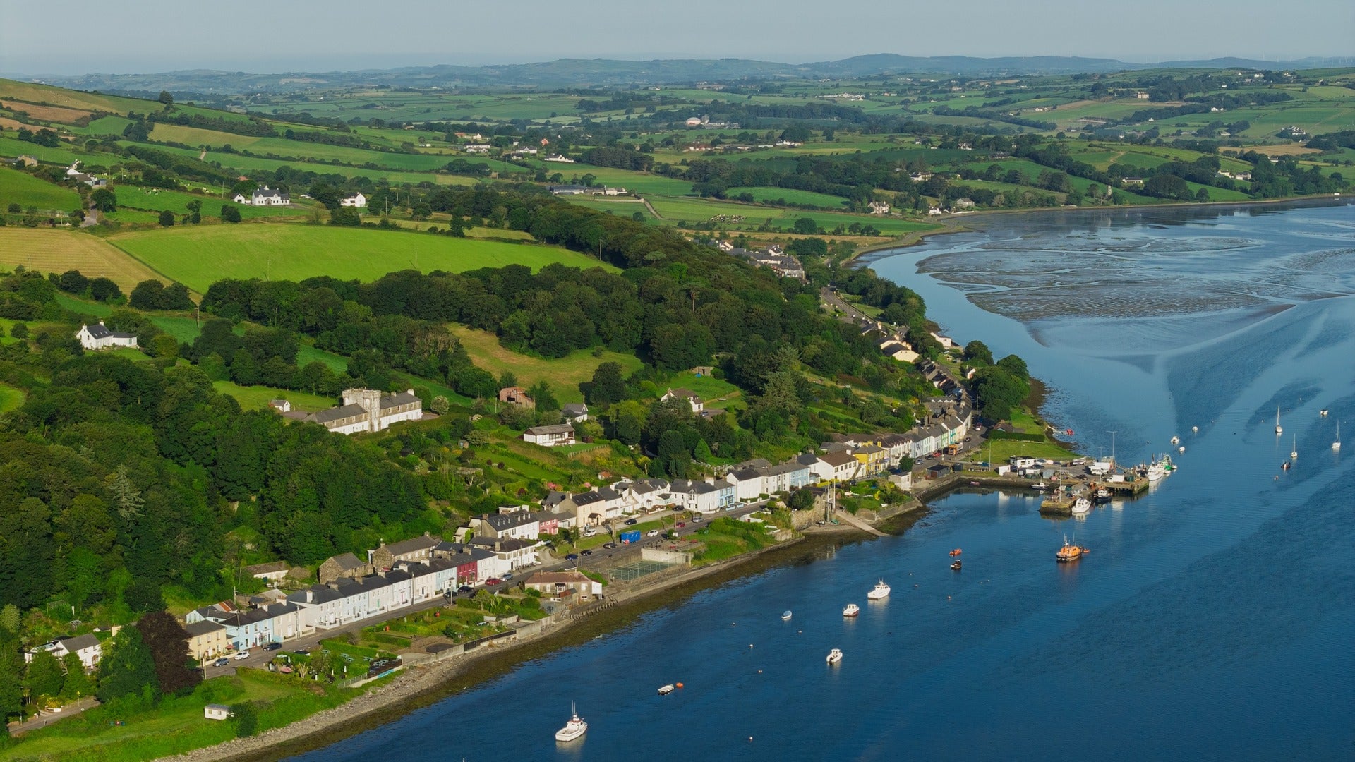 Aerial view of an Irish coastal village with colourful houses, a harbour and green countryside.