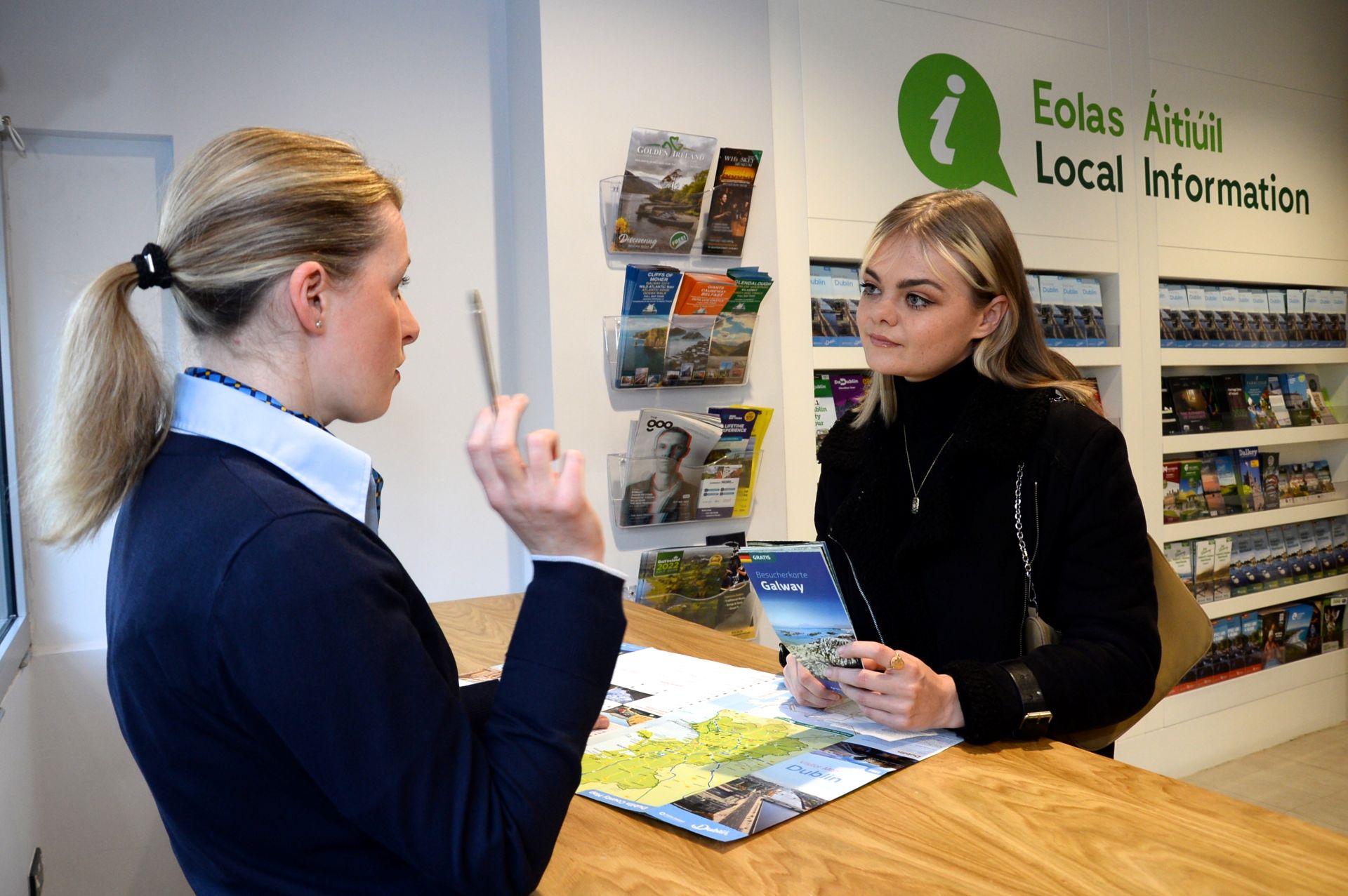 Visitor receiving assistance at a tourist information centre desk with maps and brochures