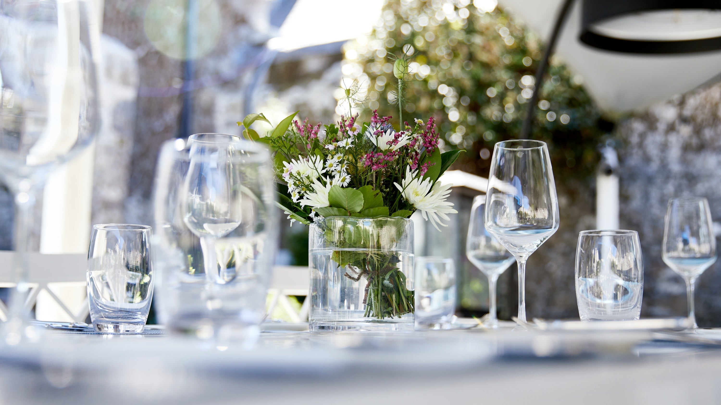 Hotel banquet staff member raising a wine glass to check its clarity in a set dining room with silver candelabras