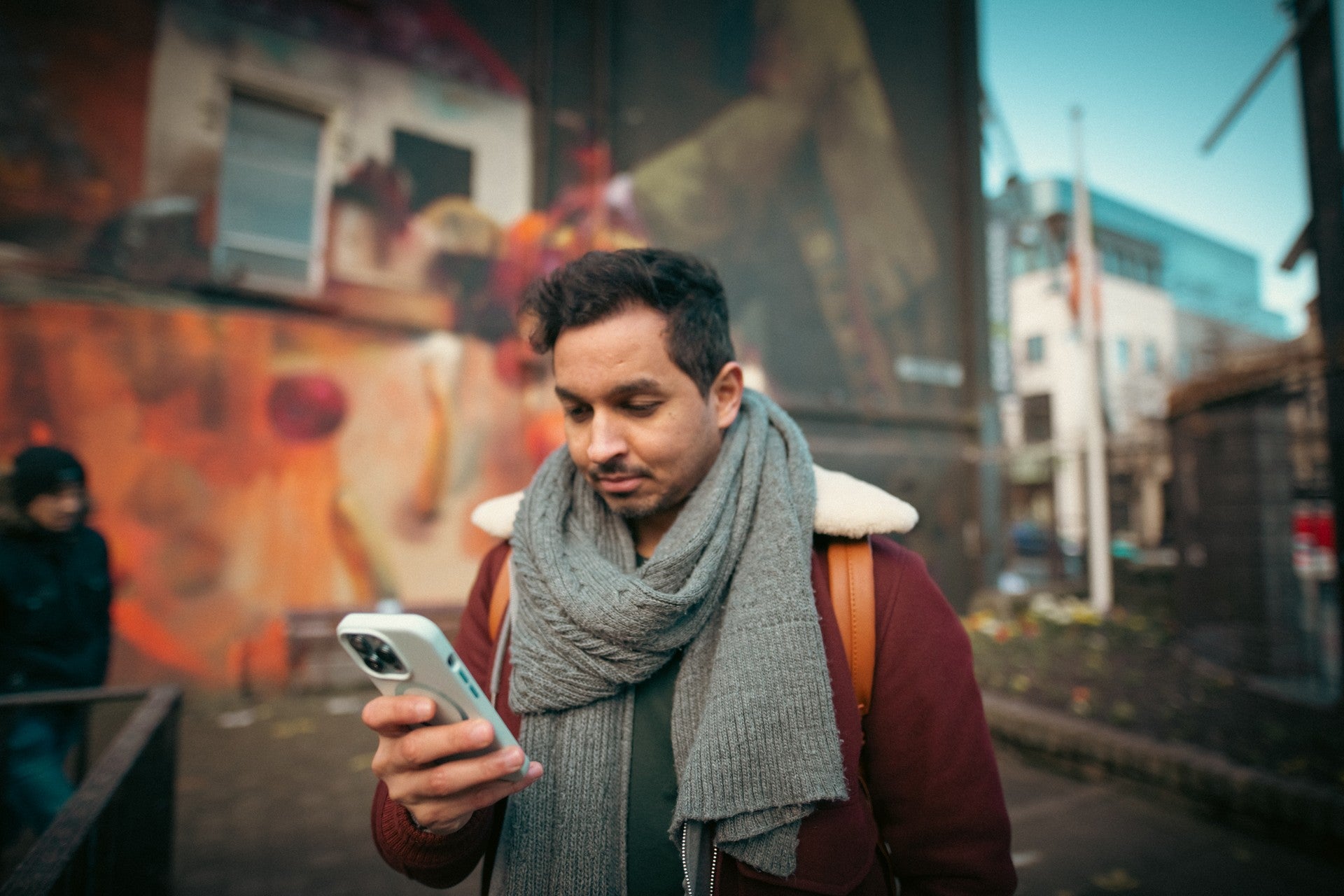Person looking at their smartphone while standing on a colourful urban street with street art in the background