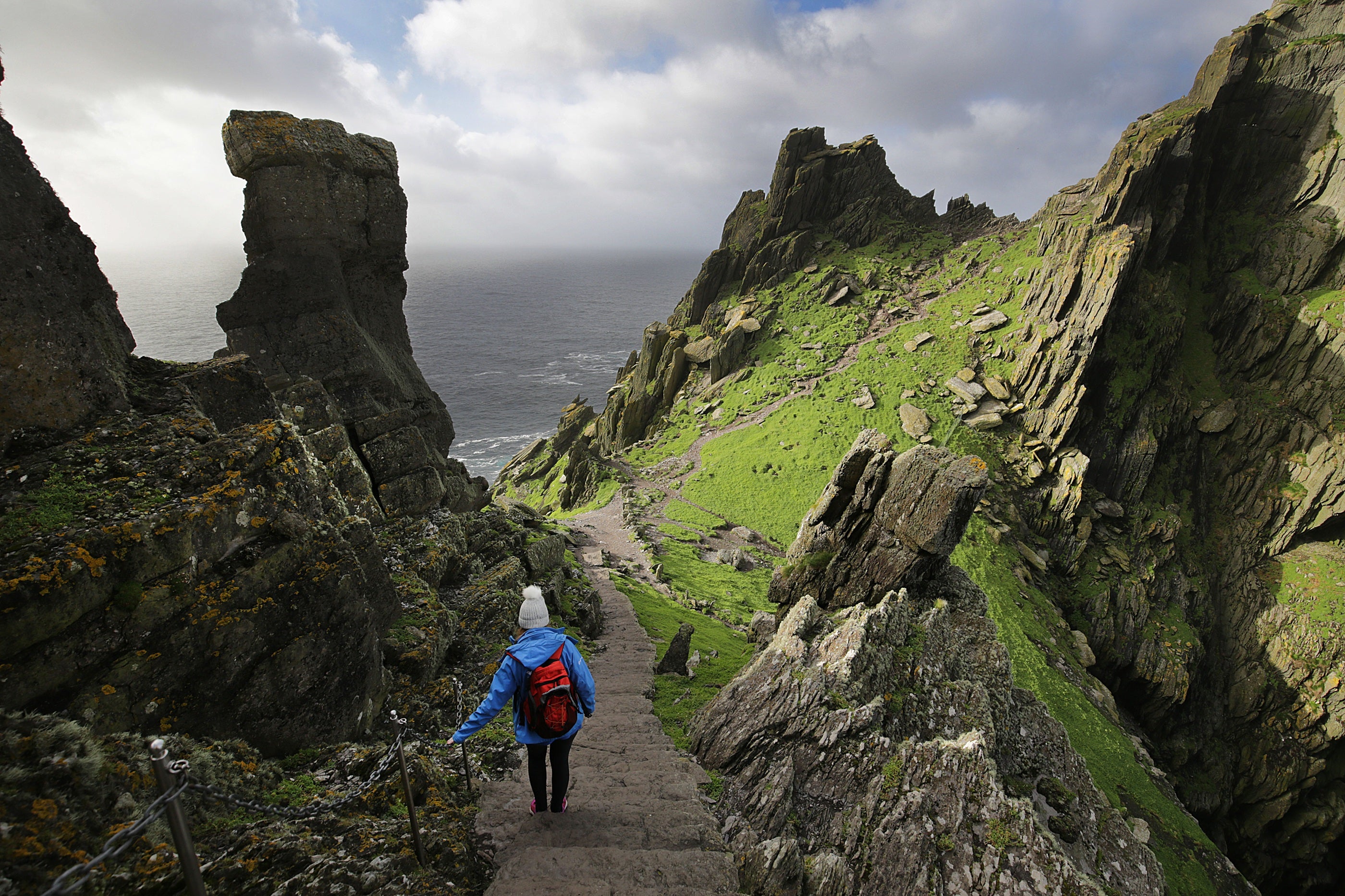 A person walking on a path with a rocky cliff and water in the background