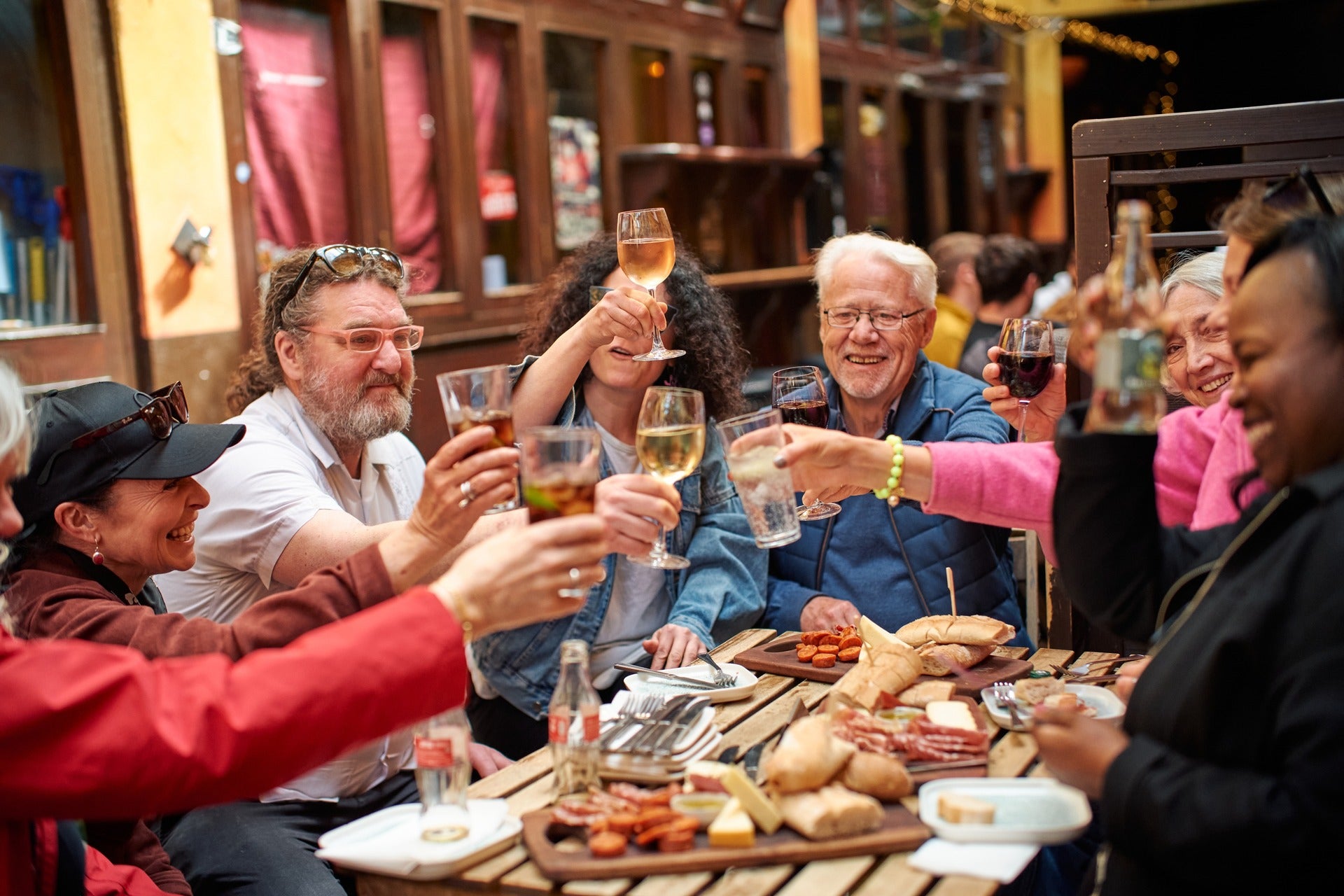Group of people raising glasses in a toast at an outdoor restaurant table with charcuterie and food boards