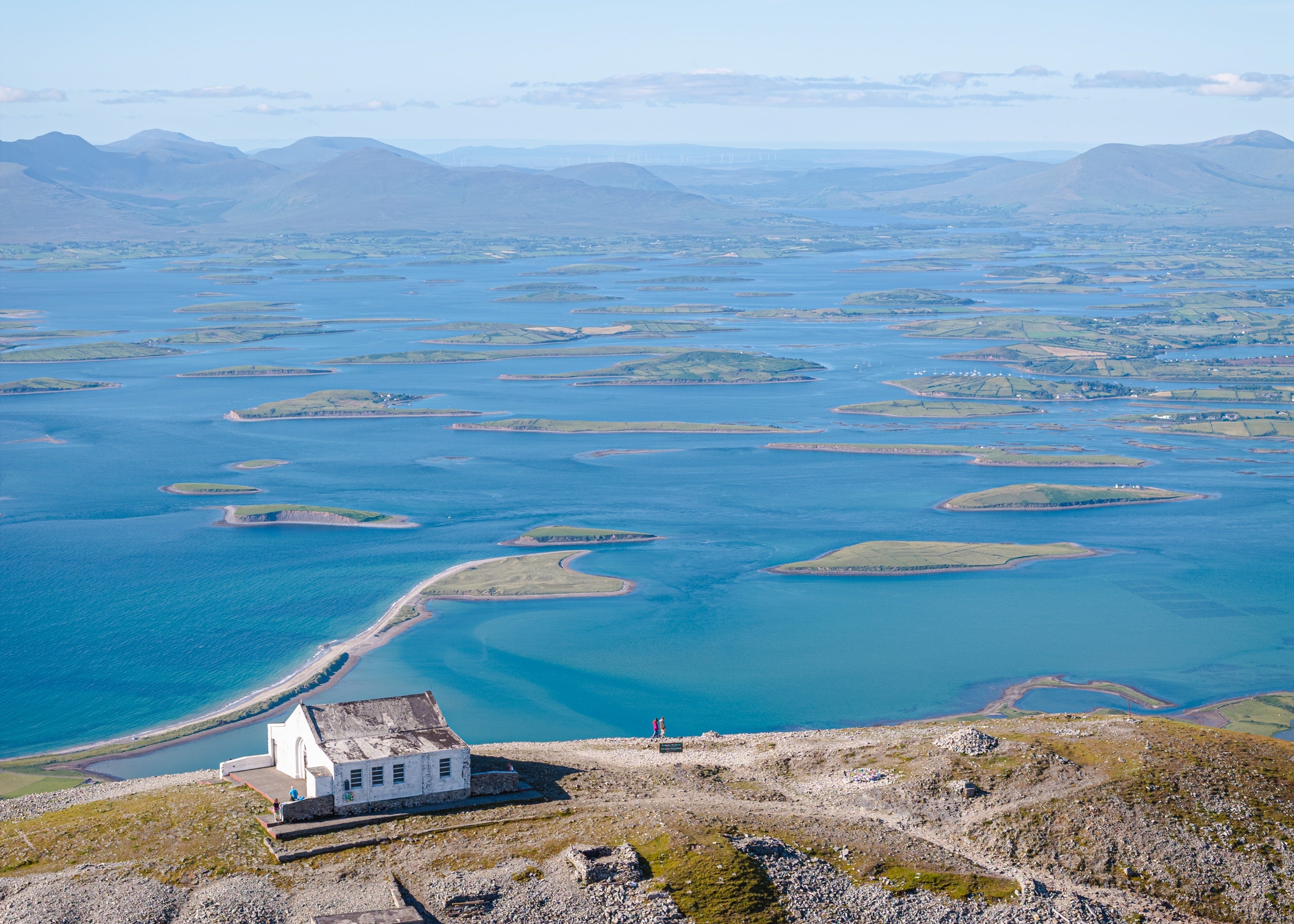 A house on a hill with water and mountains in the background