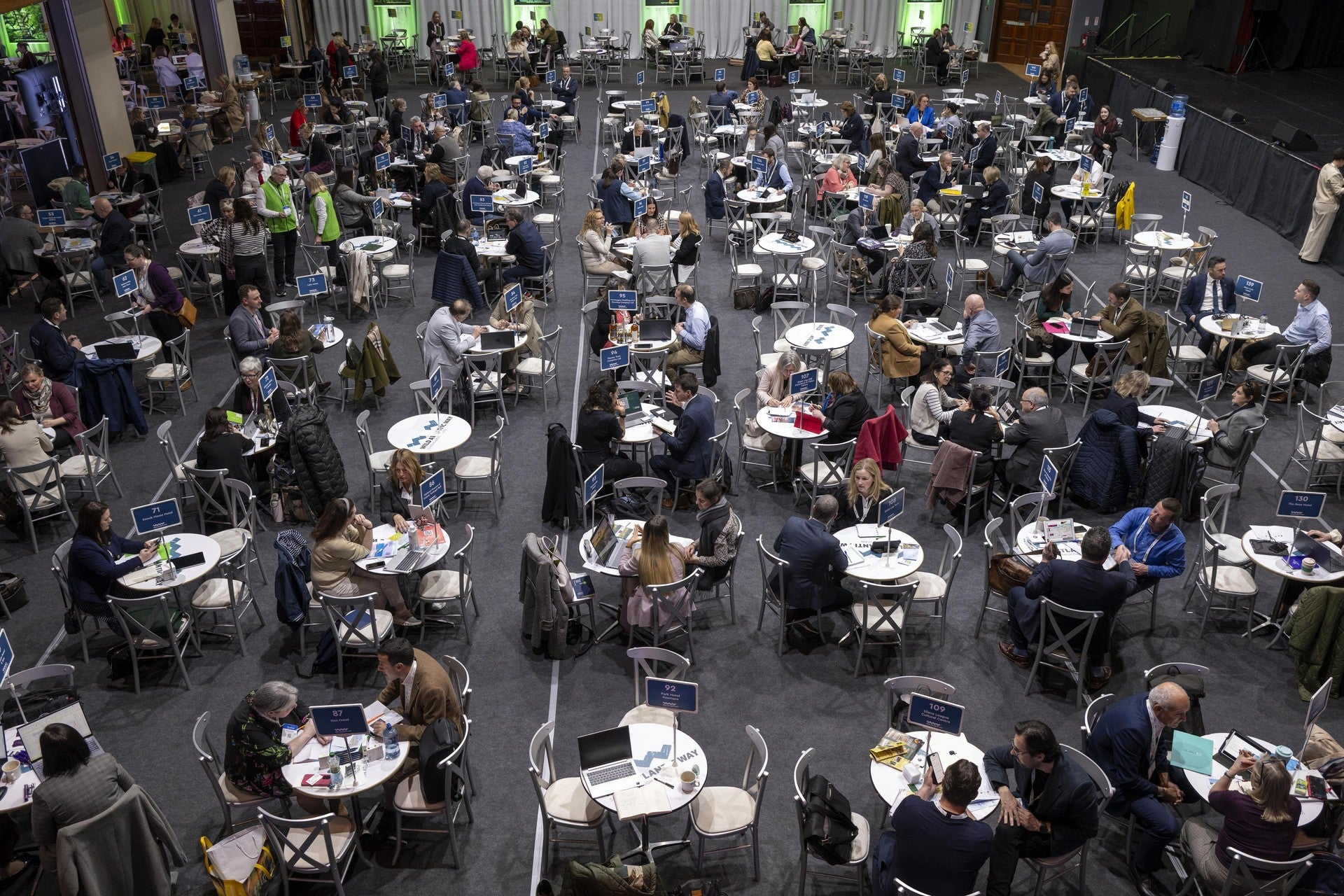 Overhead view of a large trade networking event hall with hundreds of attendees seated at round tables