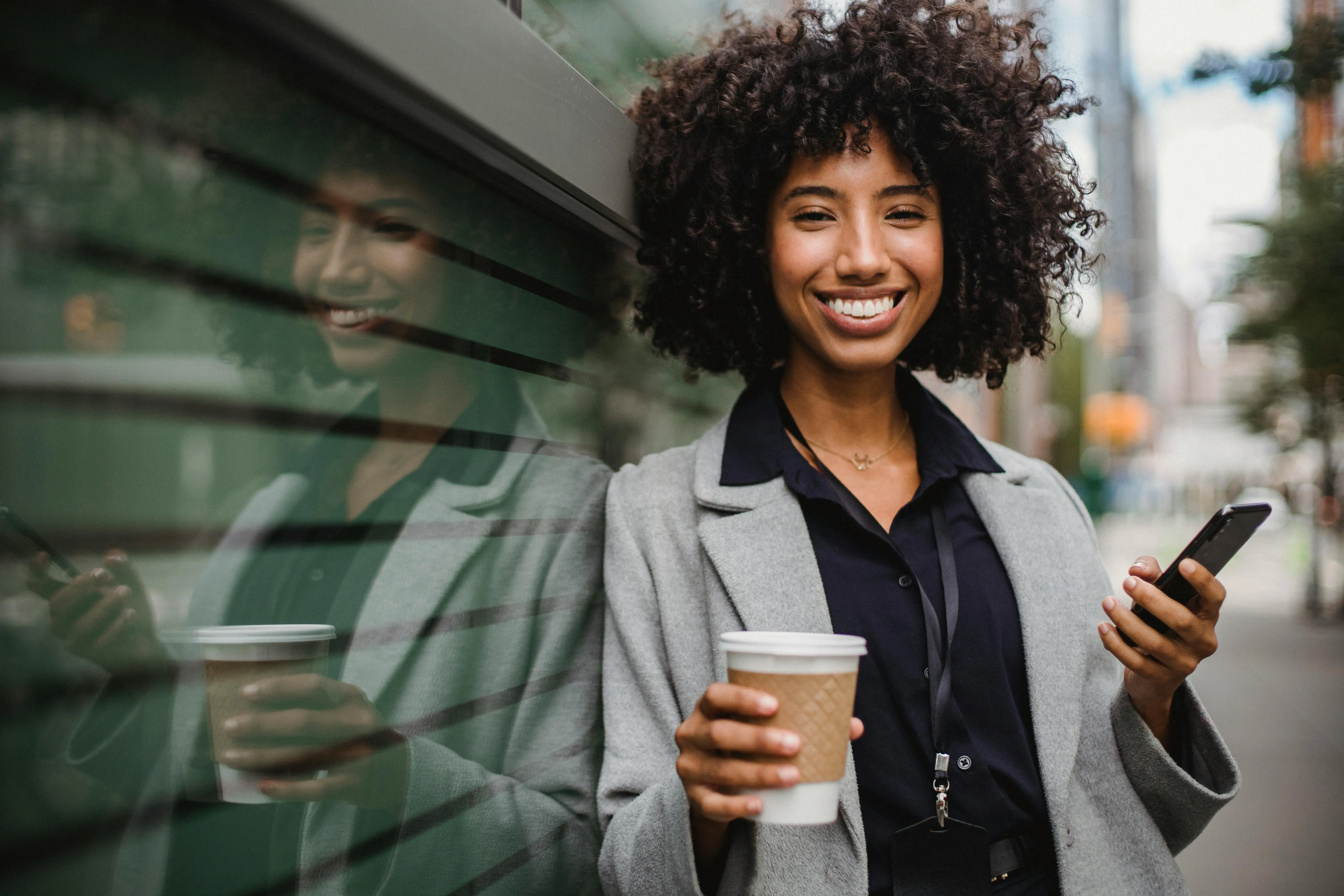 Smiling woman with coffee and phone in urban setting.