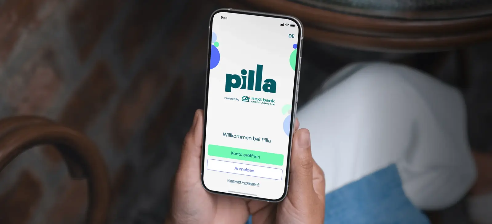 Eine Person hält ein Smartphone, das den Startbildschirm der Pilla-App.