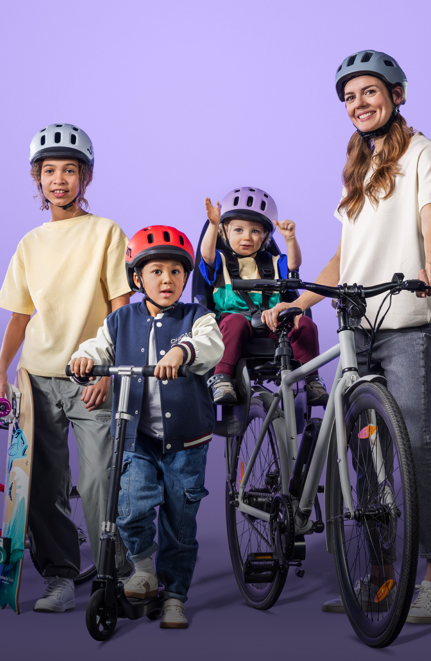 Frau mit Kleinkind im Radsitz, daneben 2 Schulkinder mit Skateboard bzw. Scooter, alle Kinder tragen den READY Helm von woom