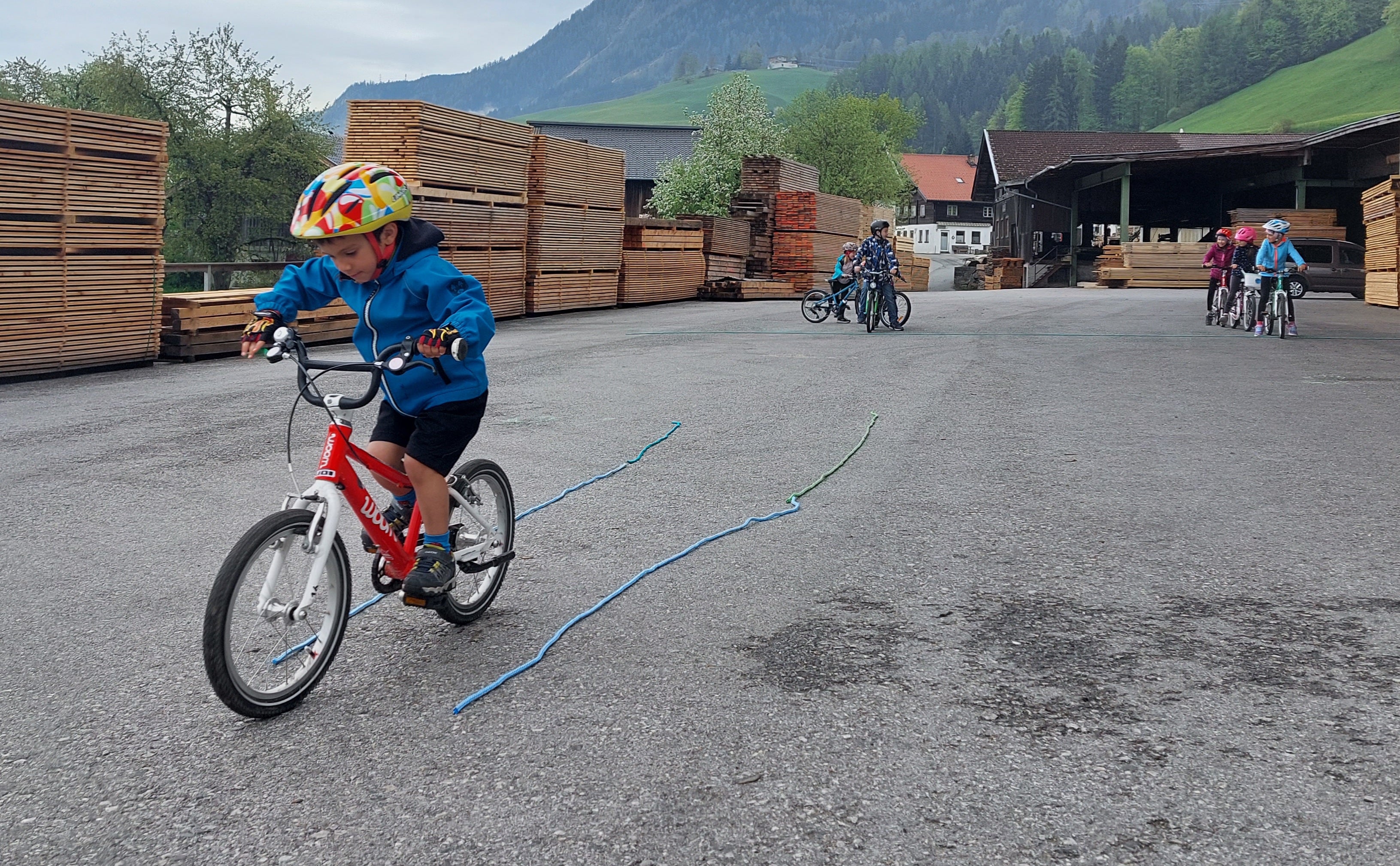 A young boy rides his woom bike in a straight line between two pieces of string laid out on the floor.
