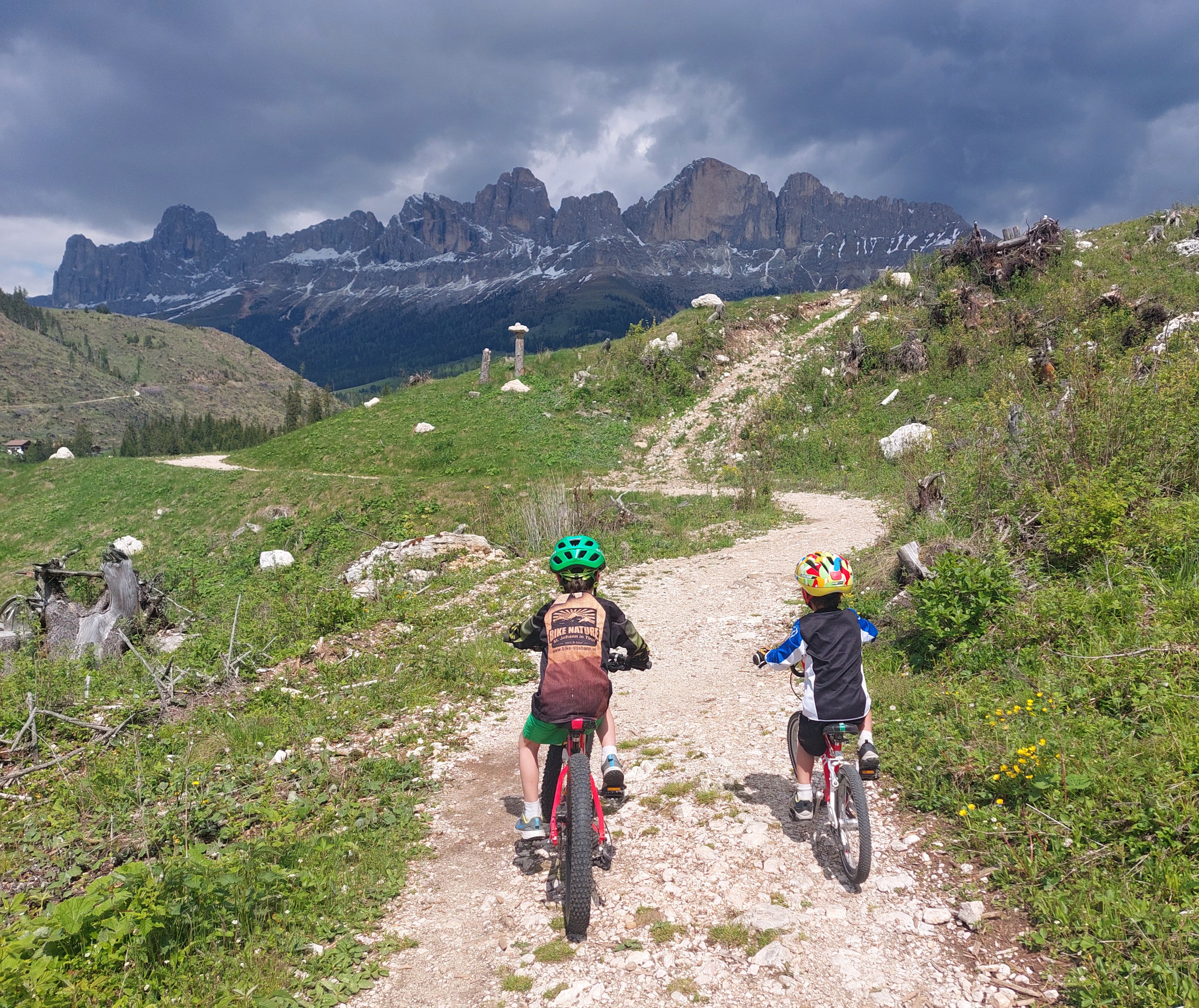 Two children cycle their woom bikes down a track in the Italian Alps.