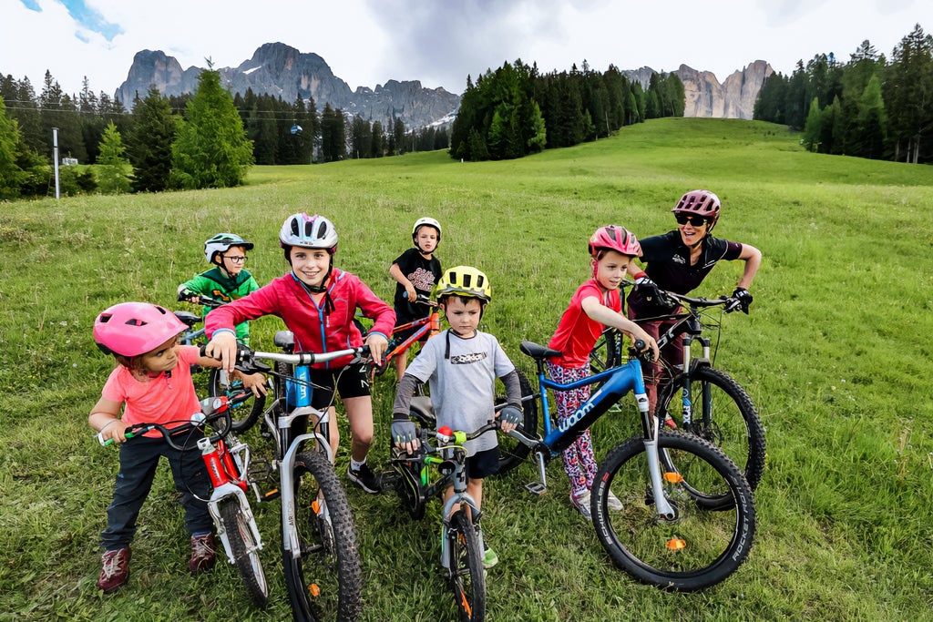 En kvinnlig cykelinstruktör och sex barn poserar med cyklar, inklusive två woom UP, framför en fantastisk bergskuliss.