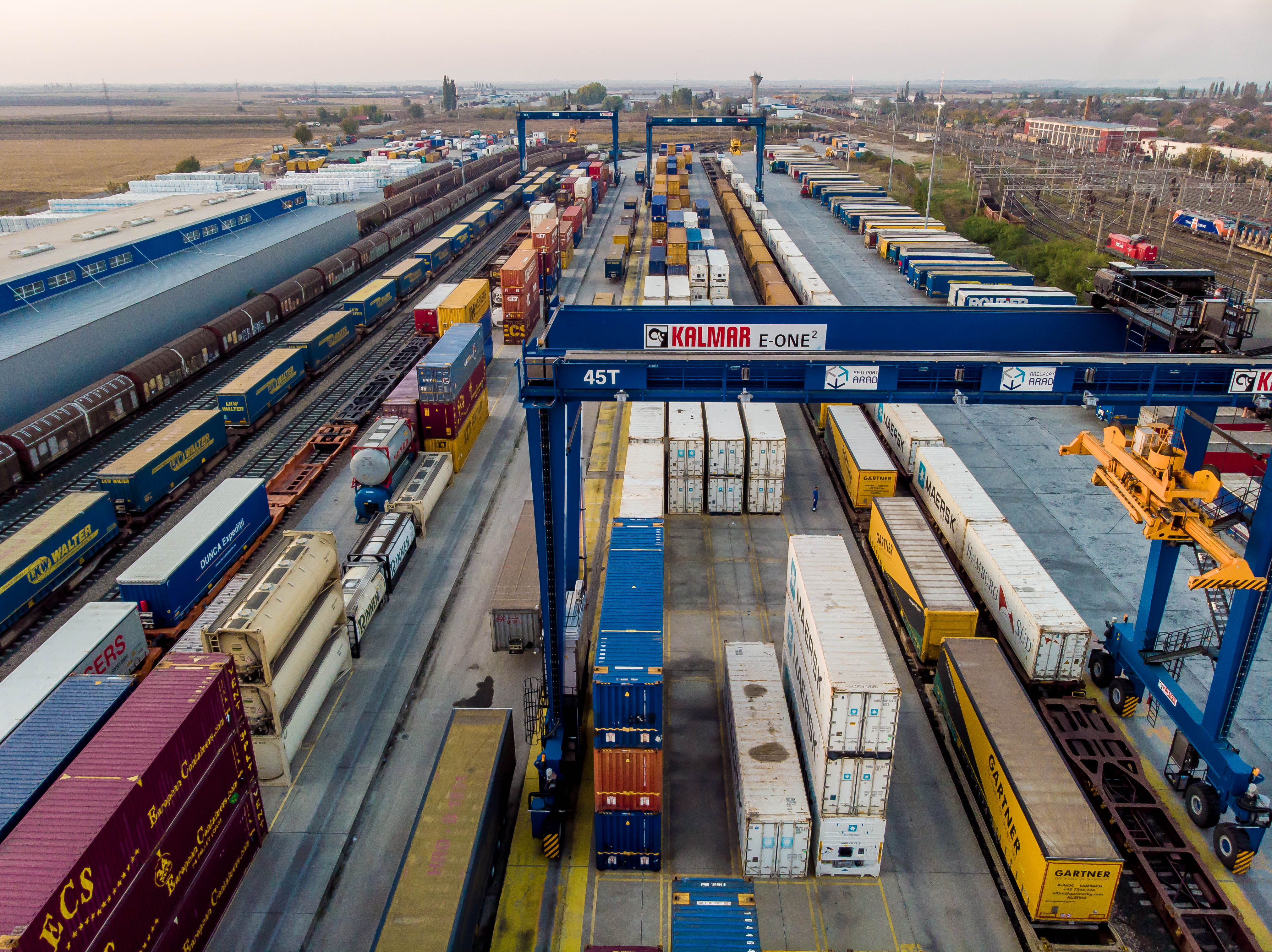 Aerial view of a busy cargo train station with multiple railway tracks and freight trains loaded with various shipping containers.