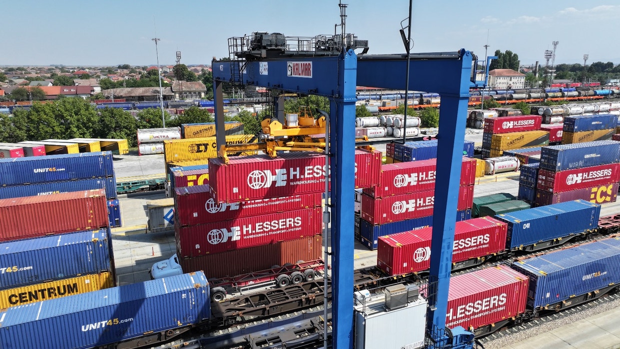 Aerial view of a busy freight terminal with colorful shipping containers and a blue gantry crane.